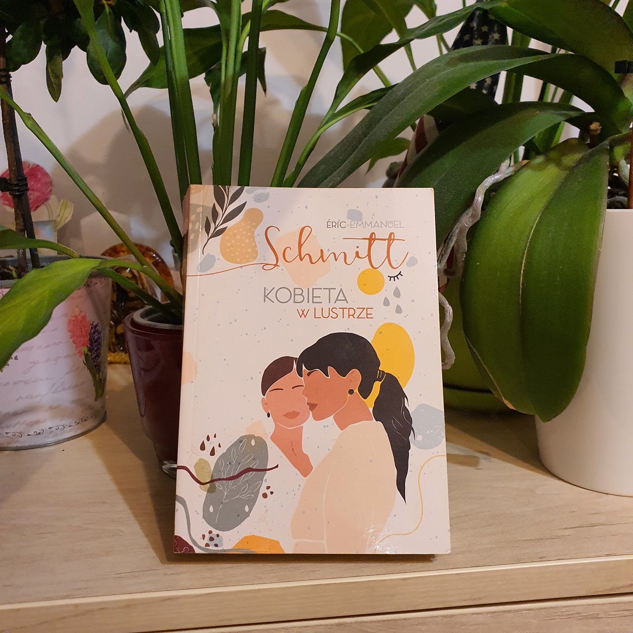 Kobieta w lustrze Eric-Emmanuel Schmitt książka wśród kwiatów doniczkowych